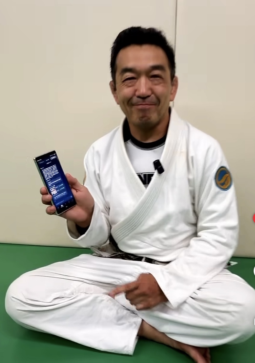 白い道着で道場に座りスマホを見せる中井祐樹氏